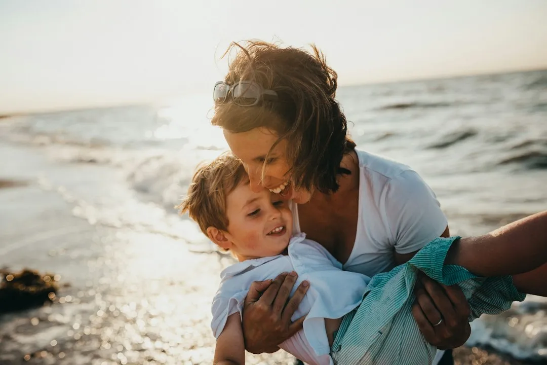 Mother holding a laughing child on a sunlit beach