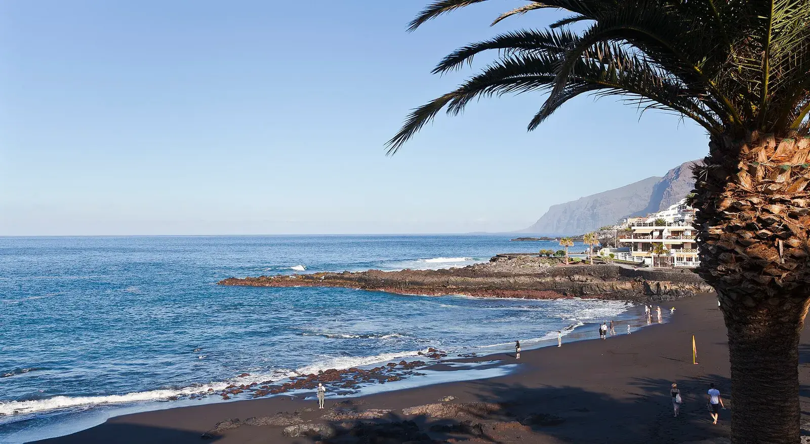 Playa de arena negra de La Arena en Puerto de Santiago, con los acantilados de Los Gigantes al fondo
