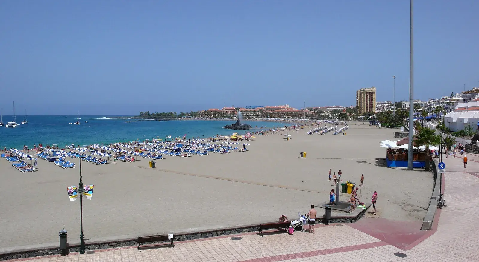 Amplia playa de Las Vistas desde el paseo, con hamacas azules, la escollera y la fuente en el mar