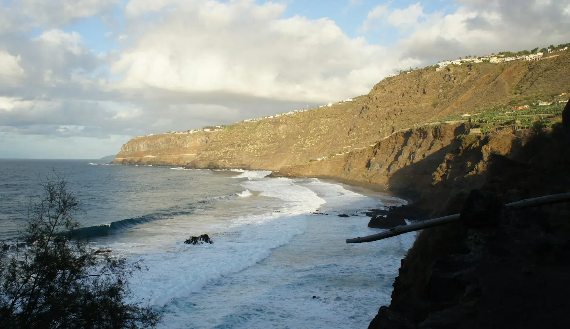 Playa de arena negra al pie de altos acantilados en la costa norte de Tenerife, con olas en la orilla