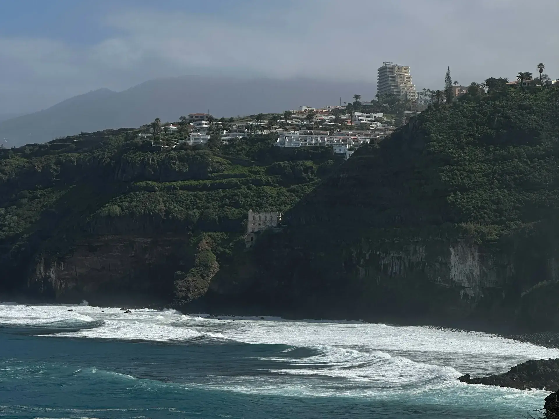 Costa norte de Tenerife con acantilados verdes y oleaje rompiendo en una playa de arena oscura