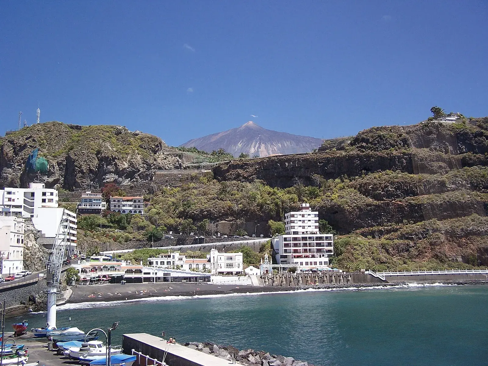 Playa de arena negra de San Marcos, con edificios blancos en el acantilado y el Teide al fondo