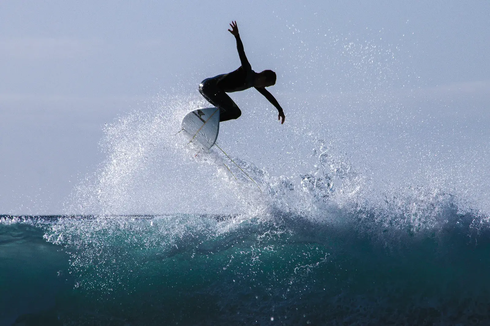 Surfista a contraluz haciendo una maniobra sobre la cresta de una ola en Tenerife