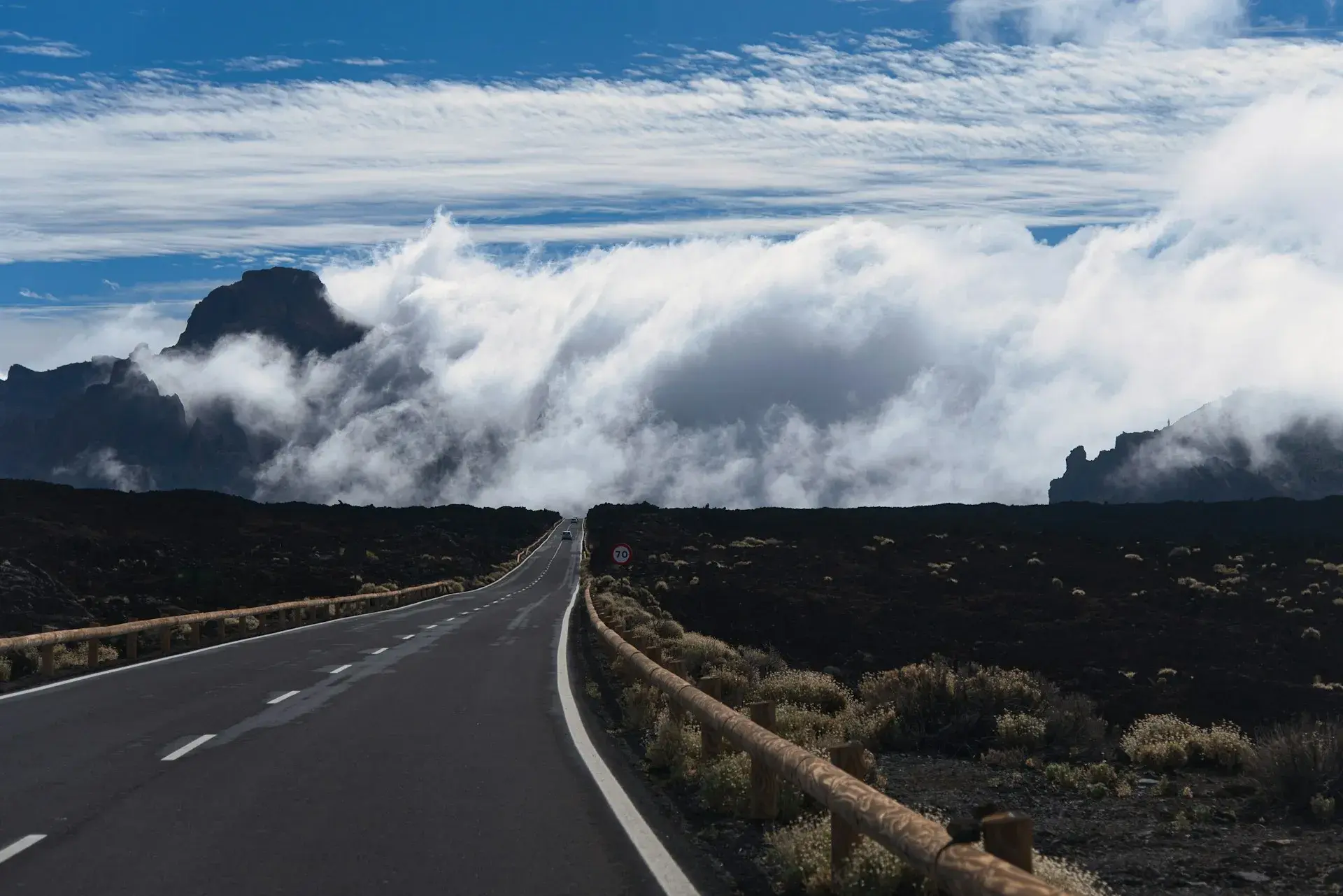 Carretera entre coladas de lava negra con nubes sobre las montañas del Parque Nacional del Teide
